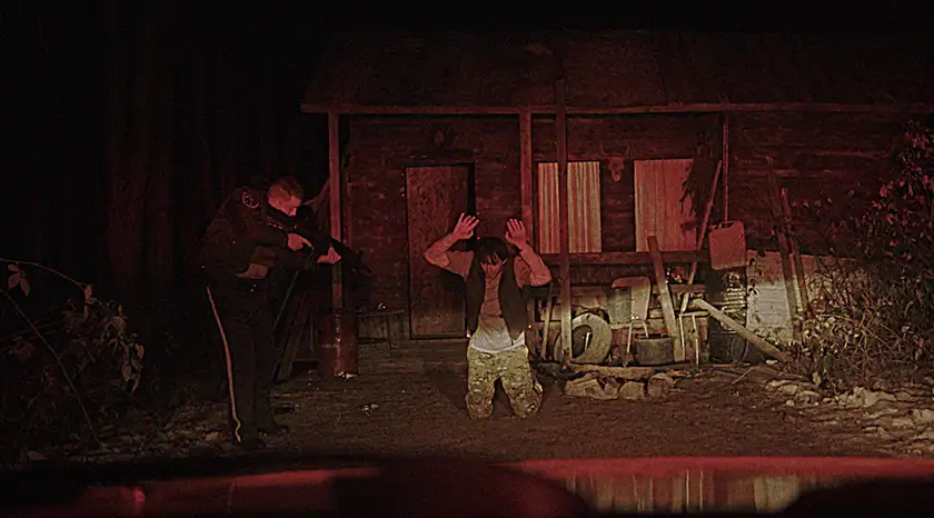 A white cop points a gun at a man with raised hands in the darkness  in the film Jericho Ridge