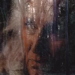 The face of a woman is overlayed on a shot of some trees in the horror film All You Need is Death