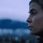 The face of a brown haired woman with blue eyes is seen on the right of the frame, looking ahead, with the mountains behind her, in the 2024 film New Life