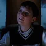 A young kid watches as a shower of frogs takes place, their shadows behind him on the wall, in a still from the movie Magnolia, which explores the theme of hope